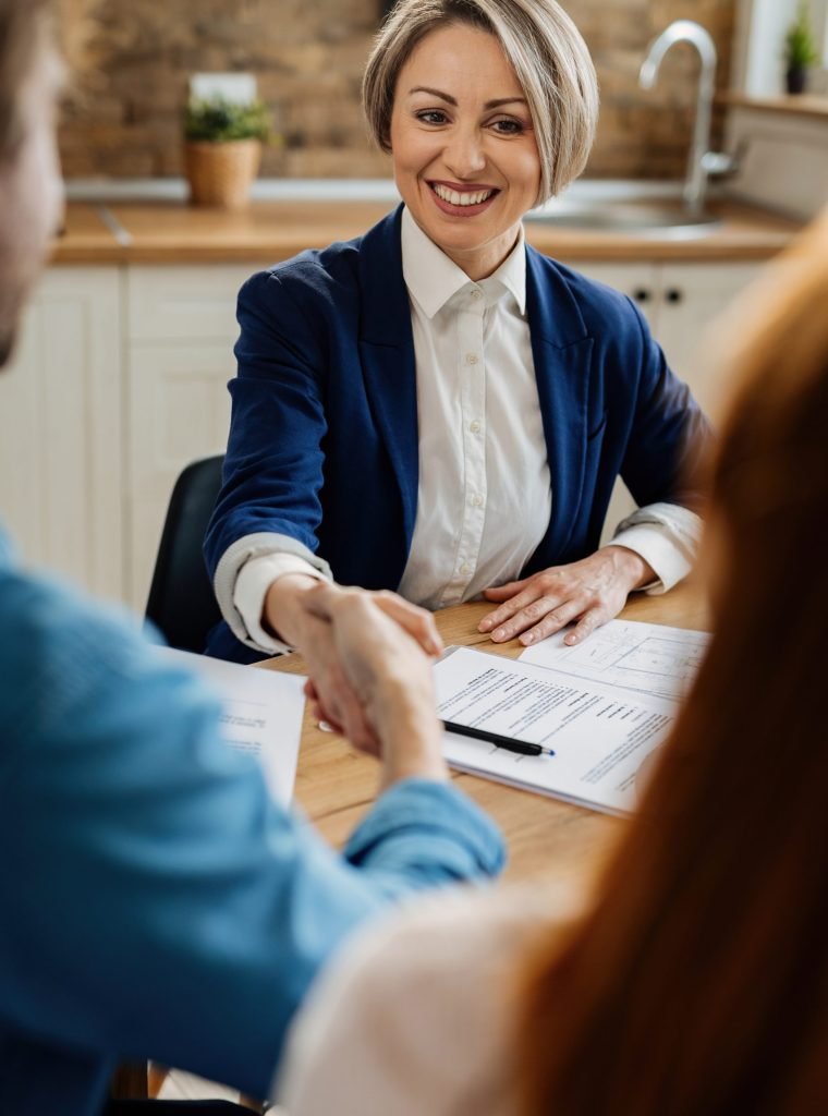 Happy insurance agent shaking hands with unrecognizable couple after the meeting.